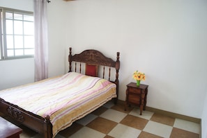 A bedroom with a wooden bed, a small bedside table with a vase of flowers, and a window with curtains. - Hotel de La Cuesta (San José)