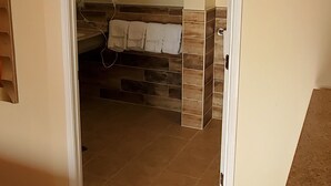 Quarto com piso de madeira, parede bege e banheiro visível por uma porta aberta.