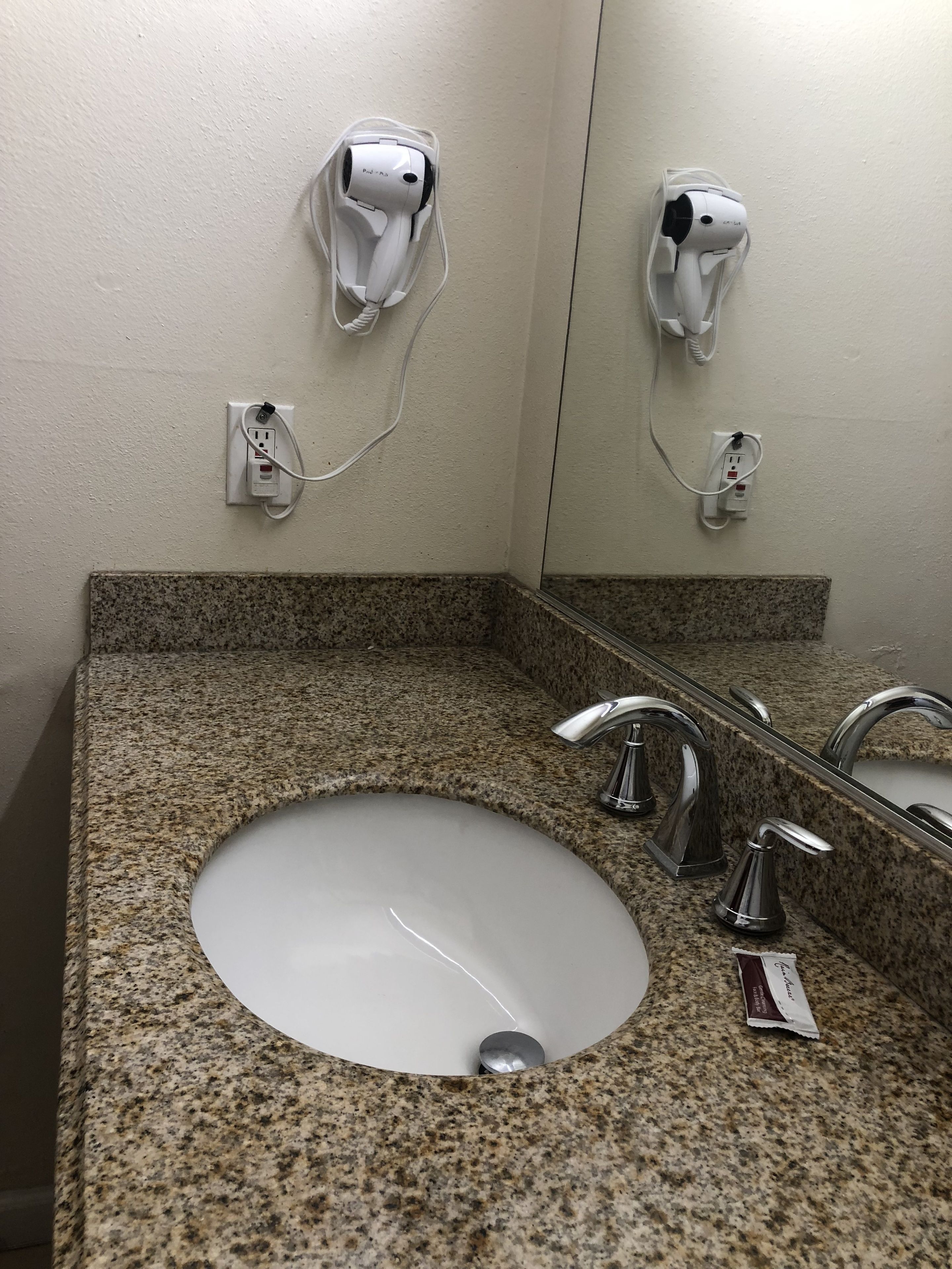 A bathroom with a granite countertop, a white sink, and two handheld hair dryers mounted on the wall.