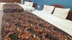 Quarto de hotel com duas camas, um edredom estampado e uma parede de destaque azul.