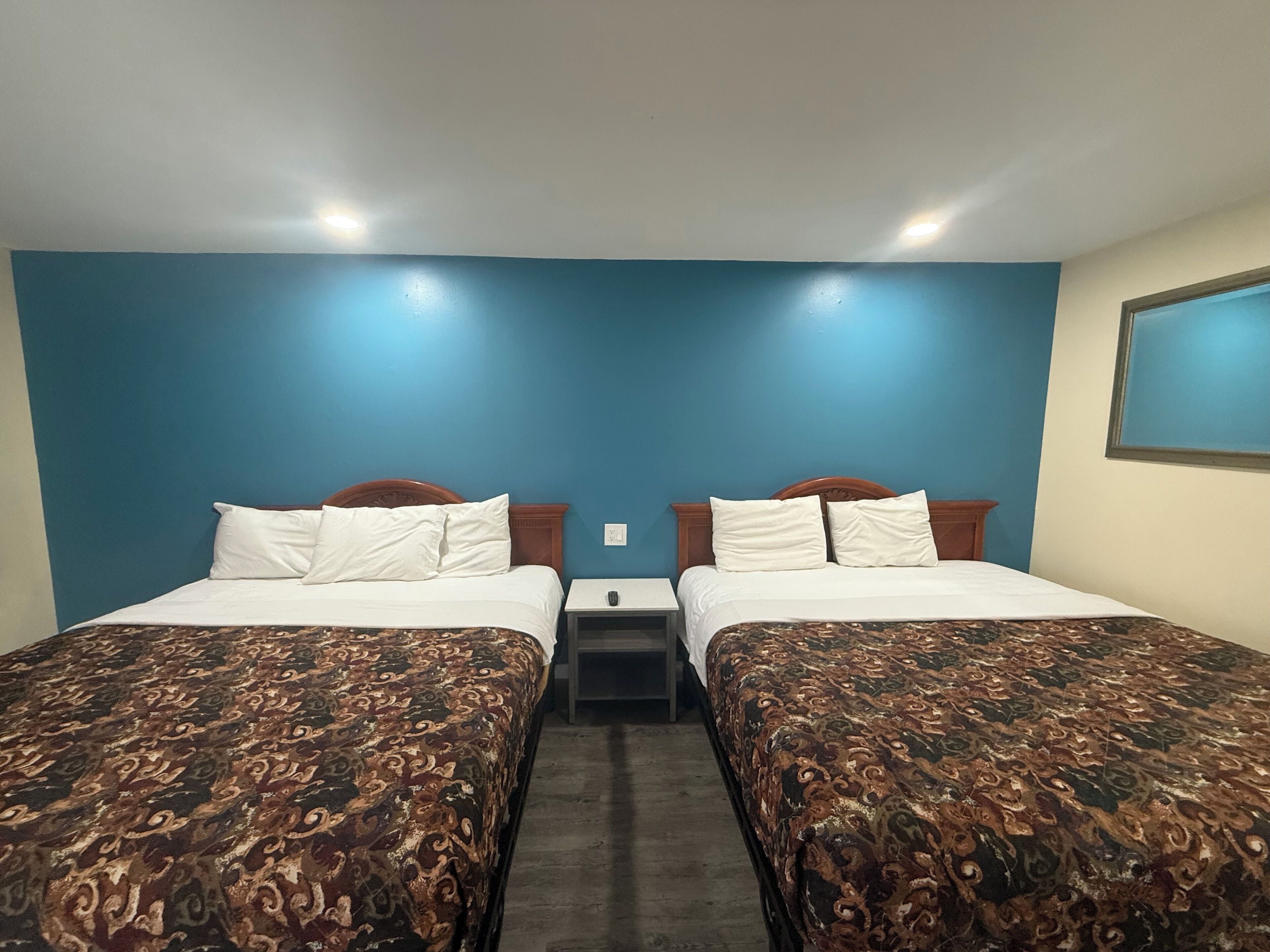 Ein Hotelzimmer mit zwei Betten, jedes mit einer gemusterten Tagesdecke, einem Nachttisch mit Lampe und einer blauen Wand.