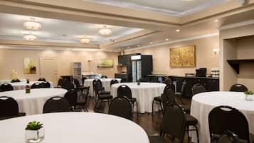 Une salle à manger d’hôtel avec plusieurs tables rondes, des chaises noires et des luminaires au plafond.