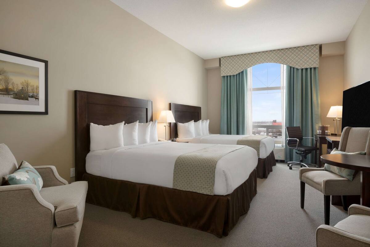 A hotel room with two beds, a desk, a chair, and a view of the city.