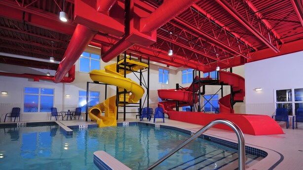 An indoor swimming pool with multiple slides and a clear pool area. - Ramada by Wyndham Emerald Park/Regina East (Emerald Park)
