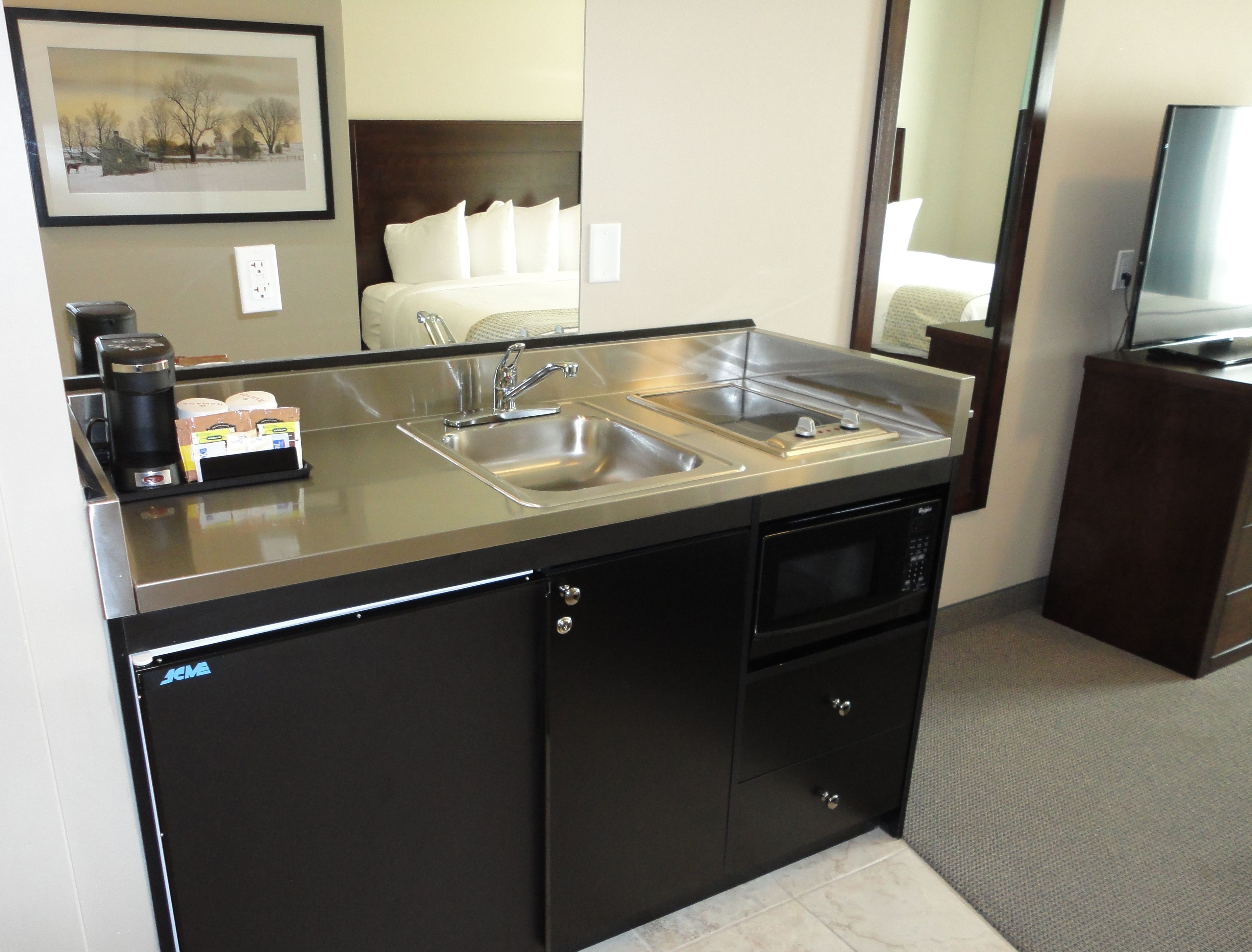 Cocina de hotel compacta con un lavamanos doble, cafetera y microondas.