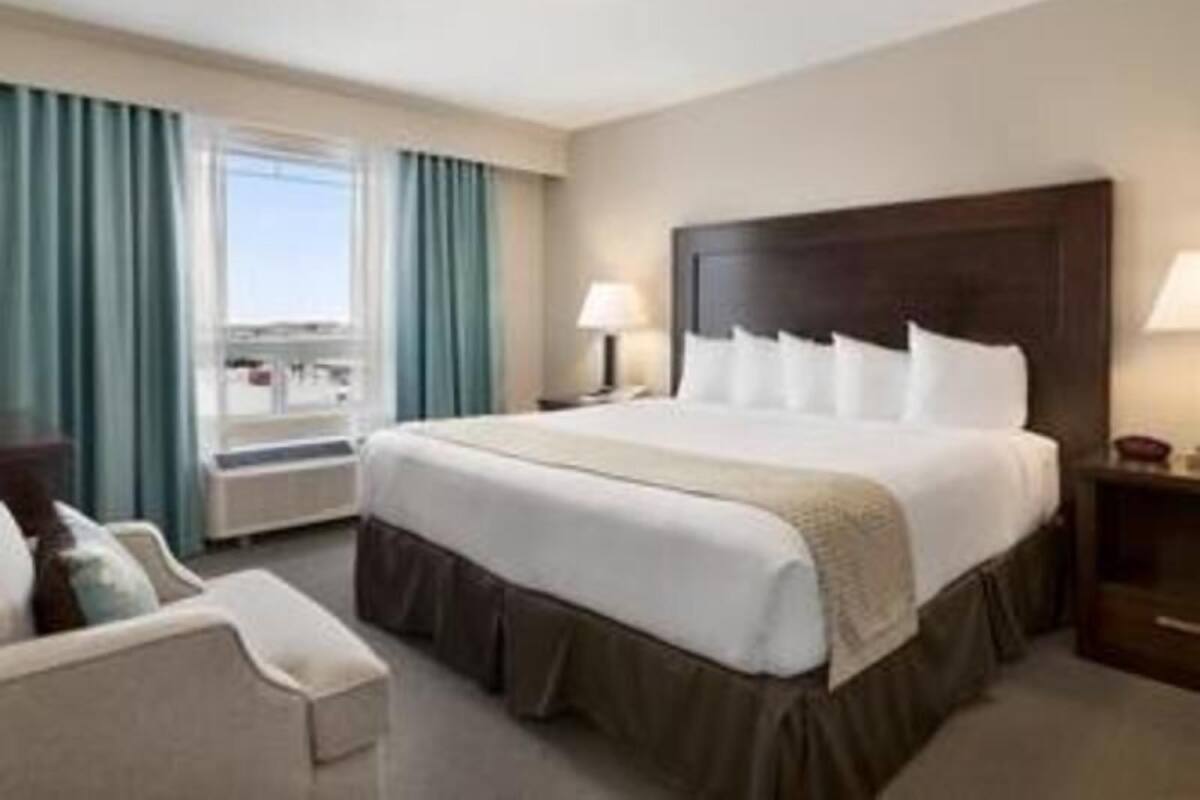 A hotel room with a large bed, a desk, a chair, a window with curtains, and a view of the outside.