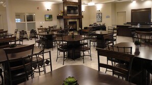 A spacious dining area with multiple tables and chairs, a fireplace, and a television mounted on the wall. - Ramada by Wyndham Emerald Park/Regina East (Emerald Park)