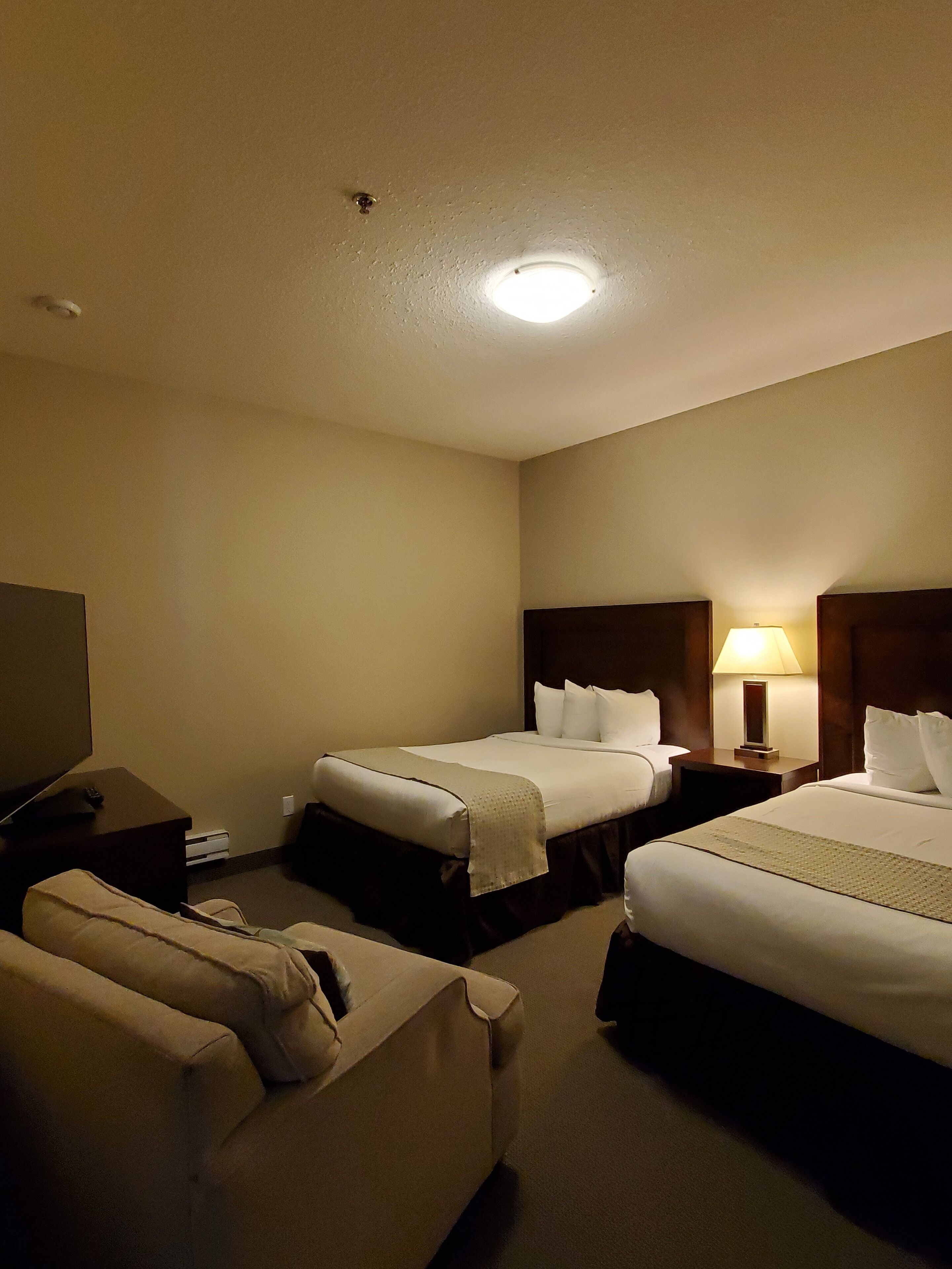 Ein Hotelzimmer mit zwei Betten, einem Fernseher, einer Lampe und einem Sofa.