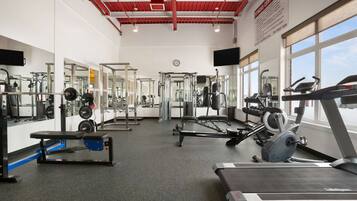 Un gimnasio con diversos equipos de ejercicio, espejos y un reloj en la pared.