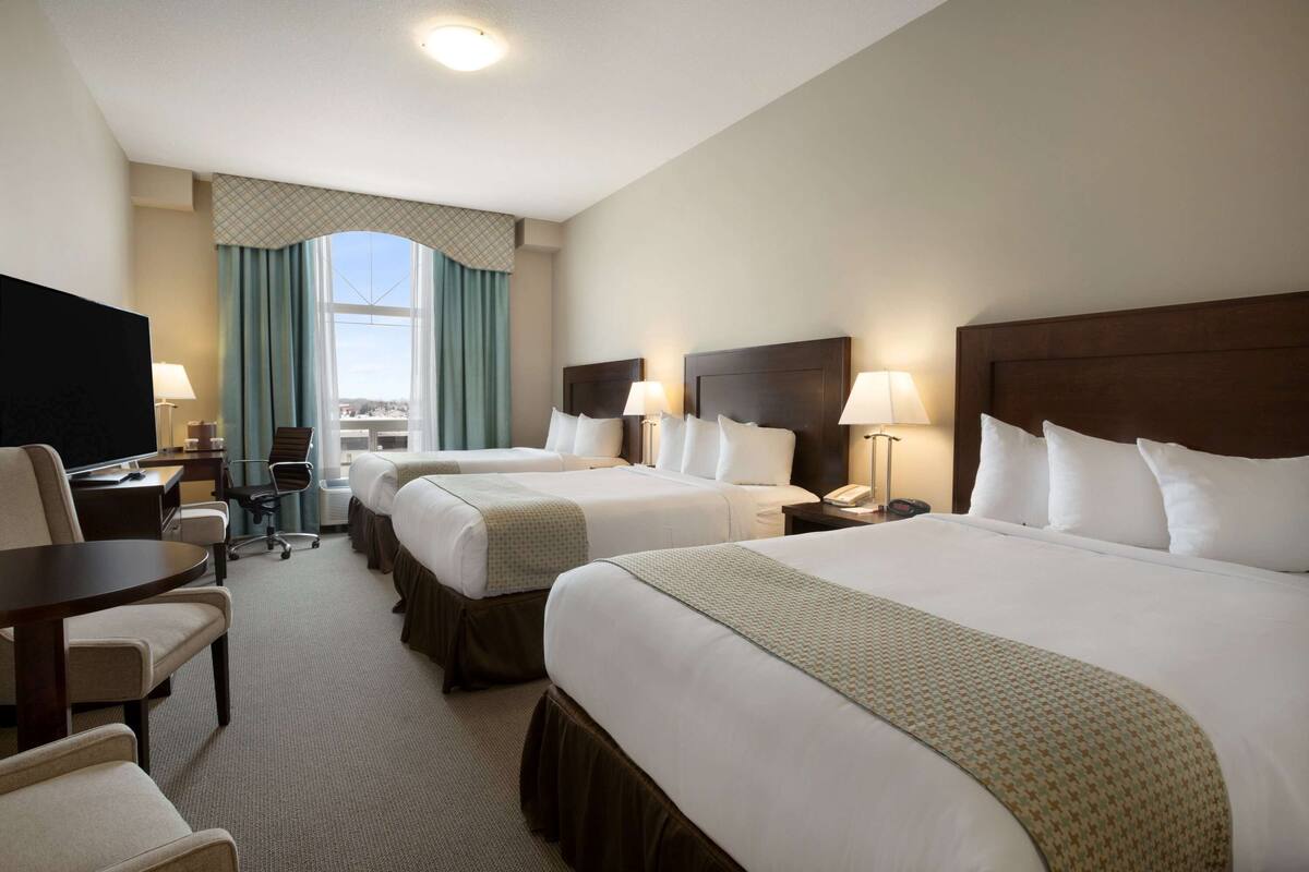 A hotel room with two beds, a desk, a chair, a TV, and a window with curtains.