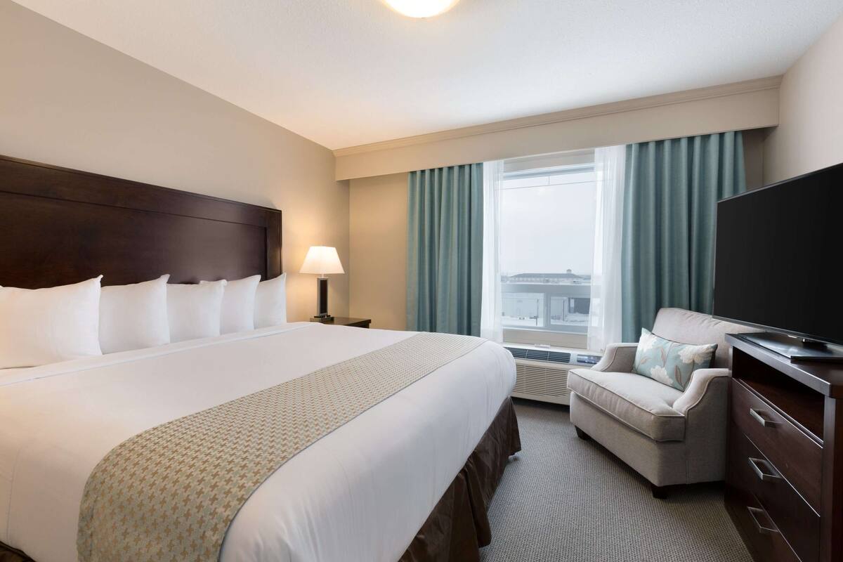 A hotel room with a large bed, a sofa, a TV, and a window with curtains.