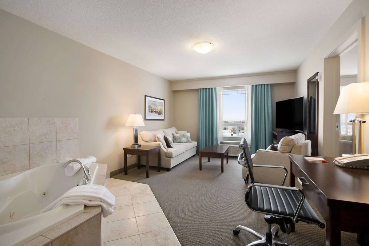 A hotel room with a bathtub, a sofa, a desk, and a television.