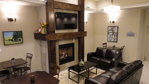 A living room with a fireplace, a television, a sofa, and a dining area. - Ramada by Wyndham Emerald Park/Regina East (Emerald Park)