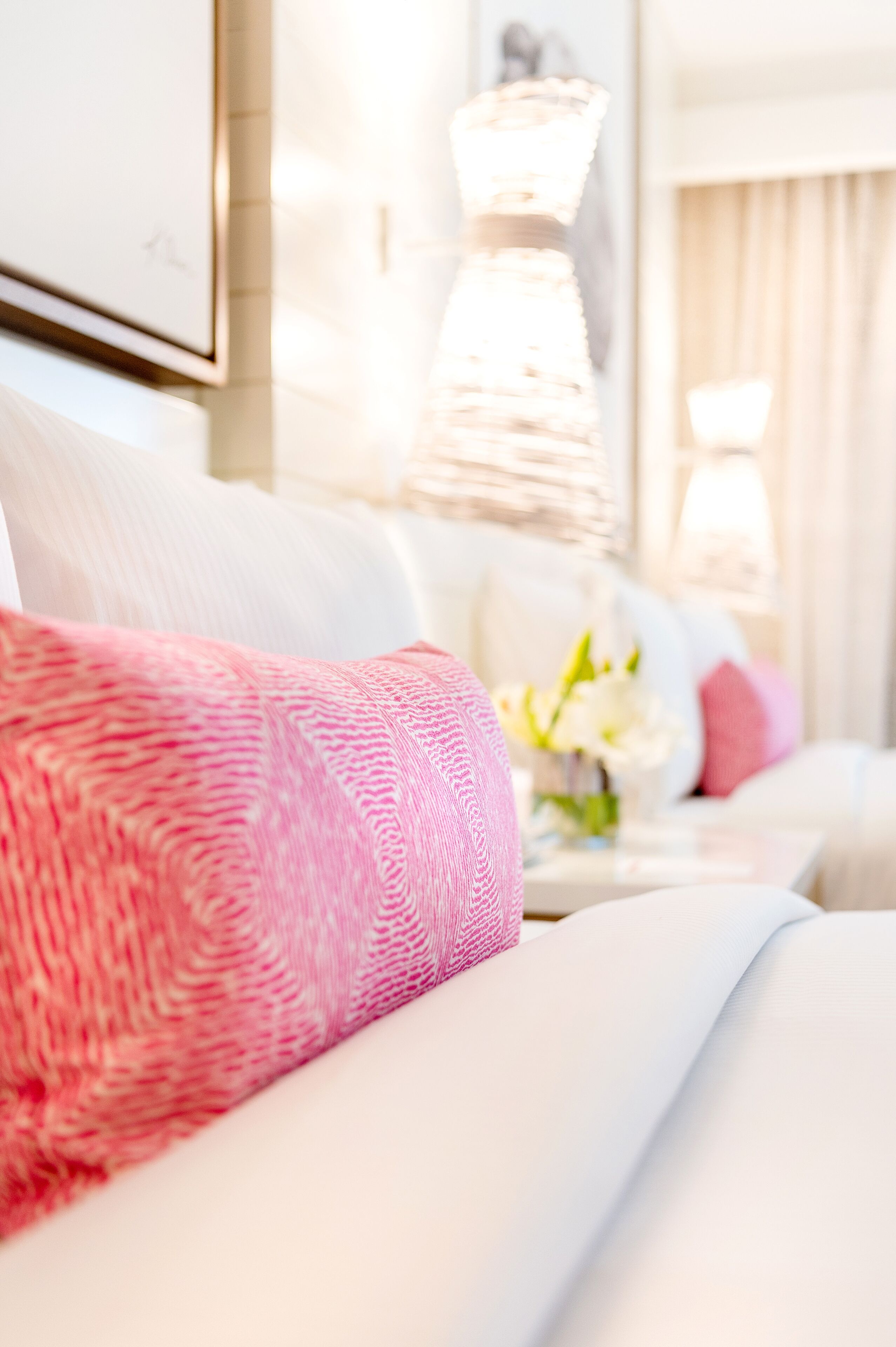 A neatly made bed with a pink textured blanket and a white pillow.
