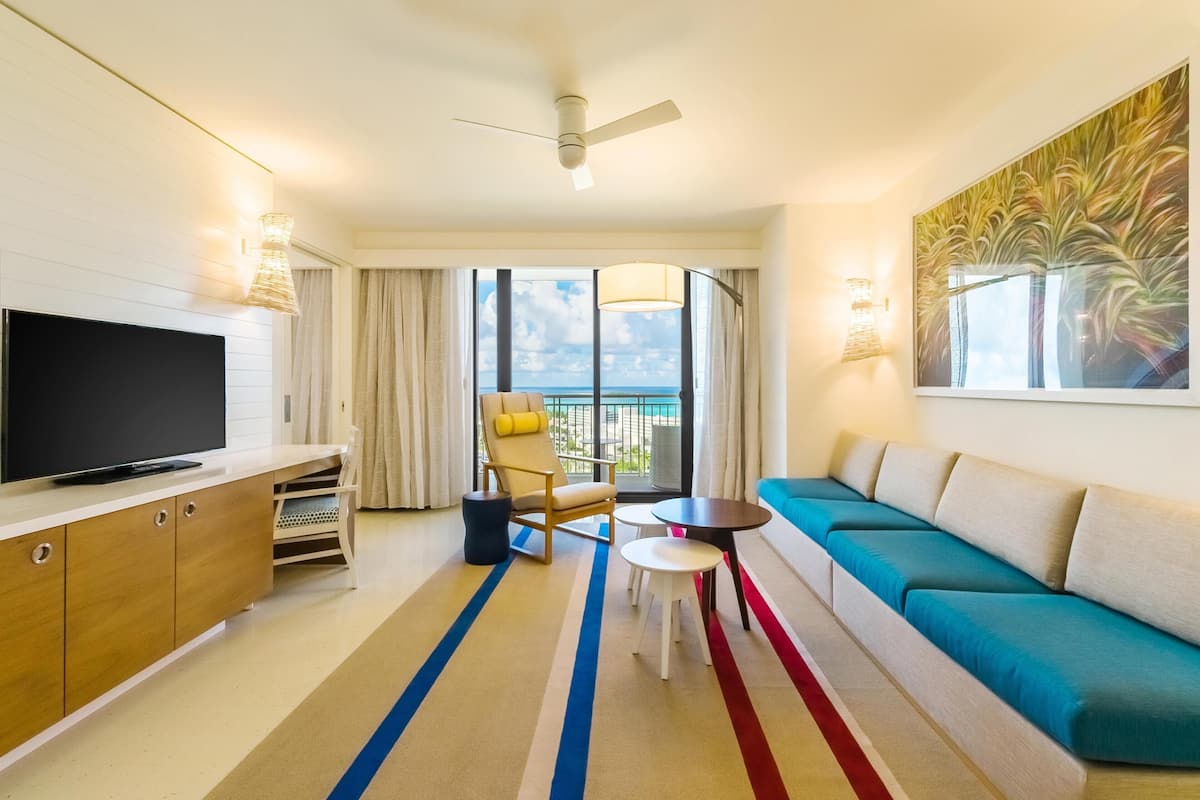 Una habitación de hotel moderna con televisor, sofá, sillón y un balcón con vistas.