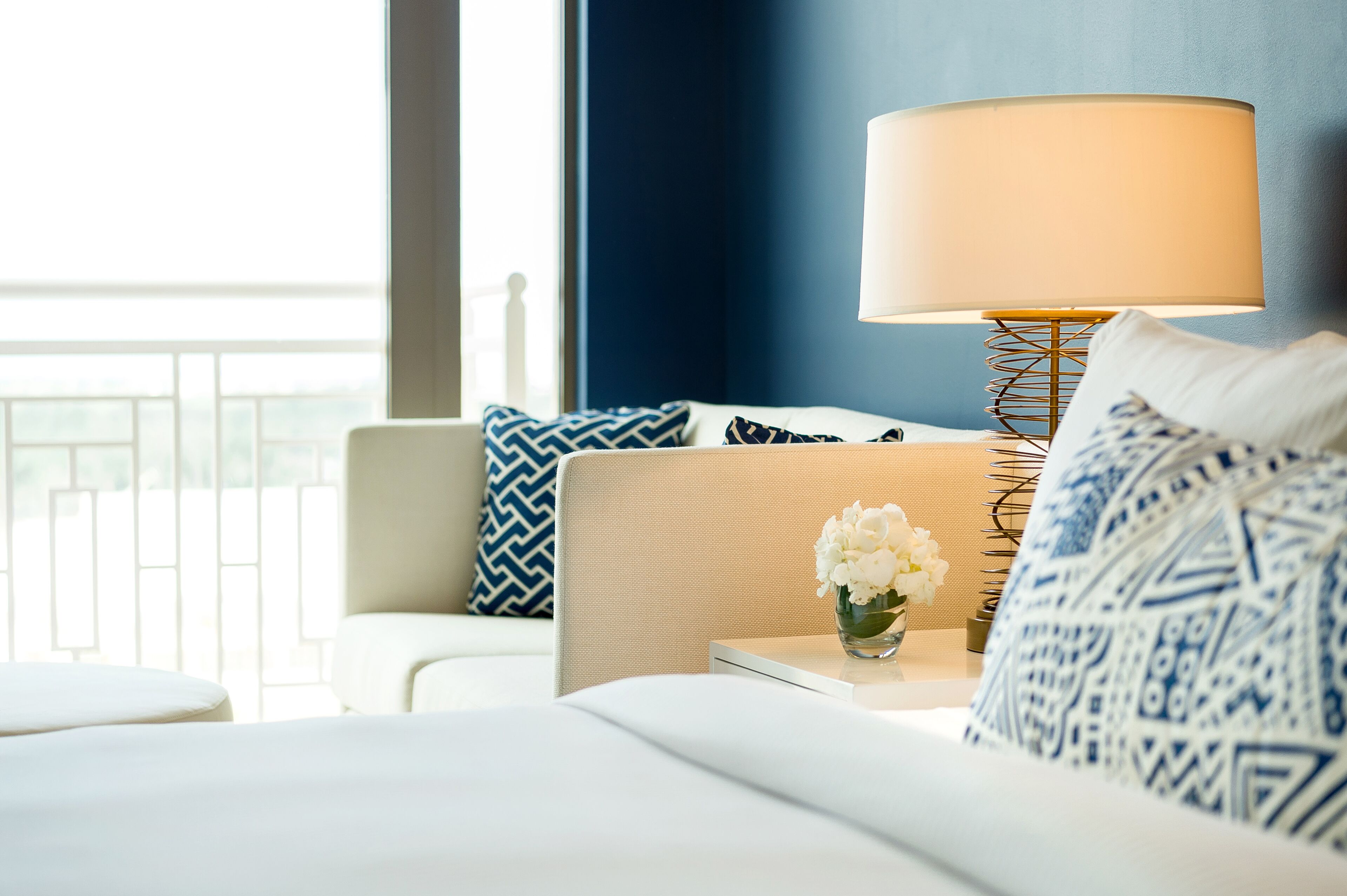 A hotel room with a bed, a nightstand, a lamp, and a view of the outdoors.