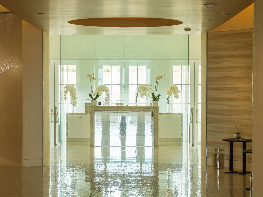 A spacious lobby with a reflective floor, a reception desk with white orchids, and a modern interior design.