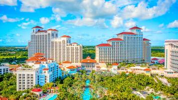 A resort with multiple high-rise buildings, a central swimming pool surrounded by palm trees, and a clear blue sky.
