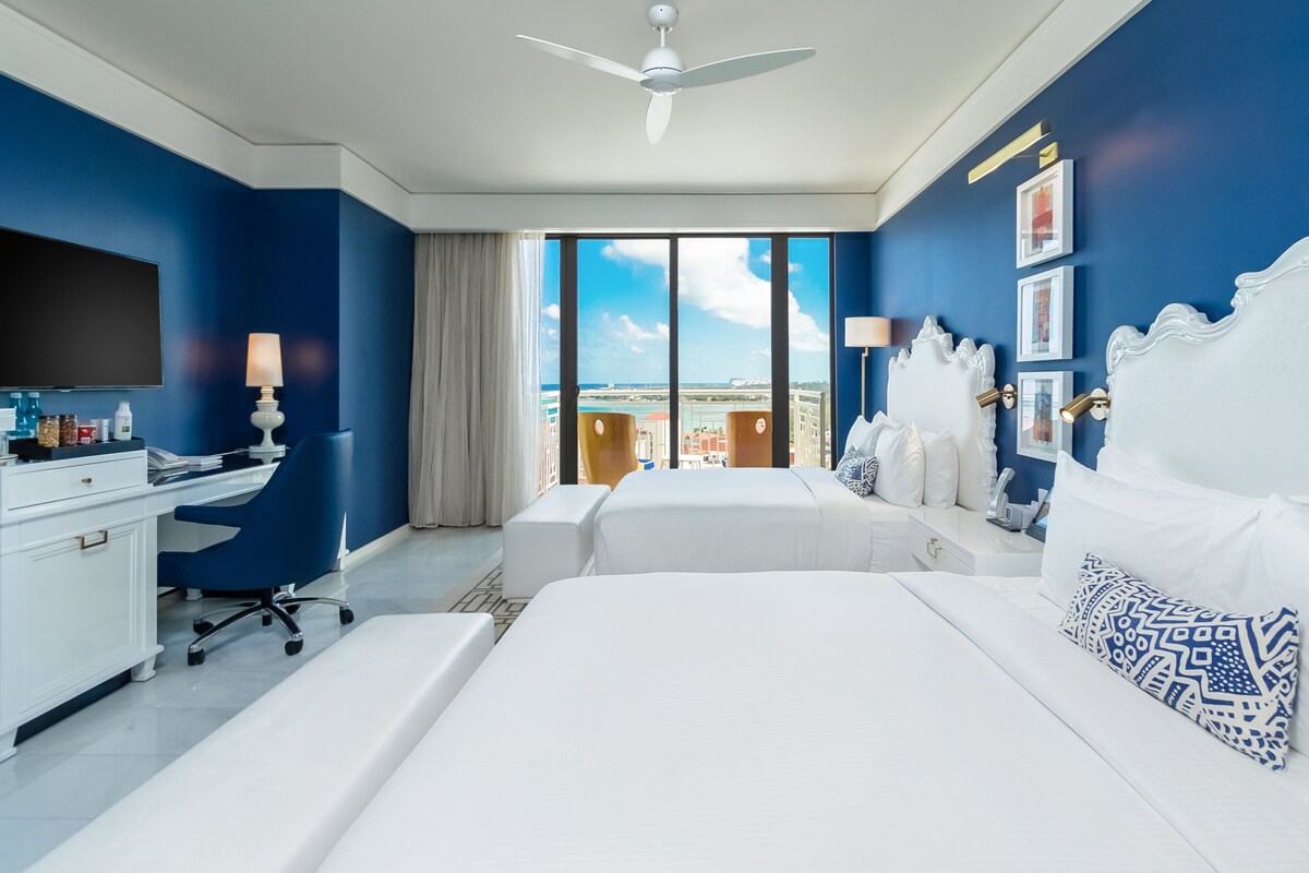 A hotel room with two beds, a desk, and a TV.