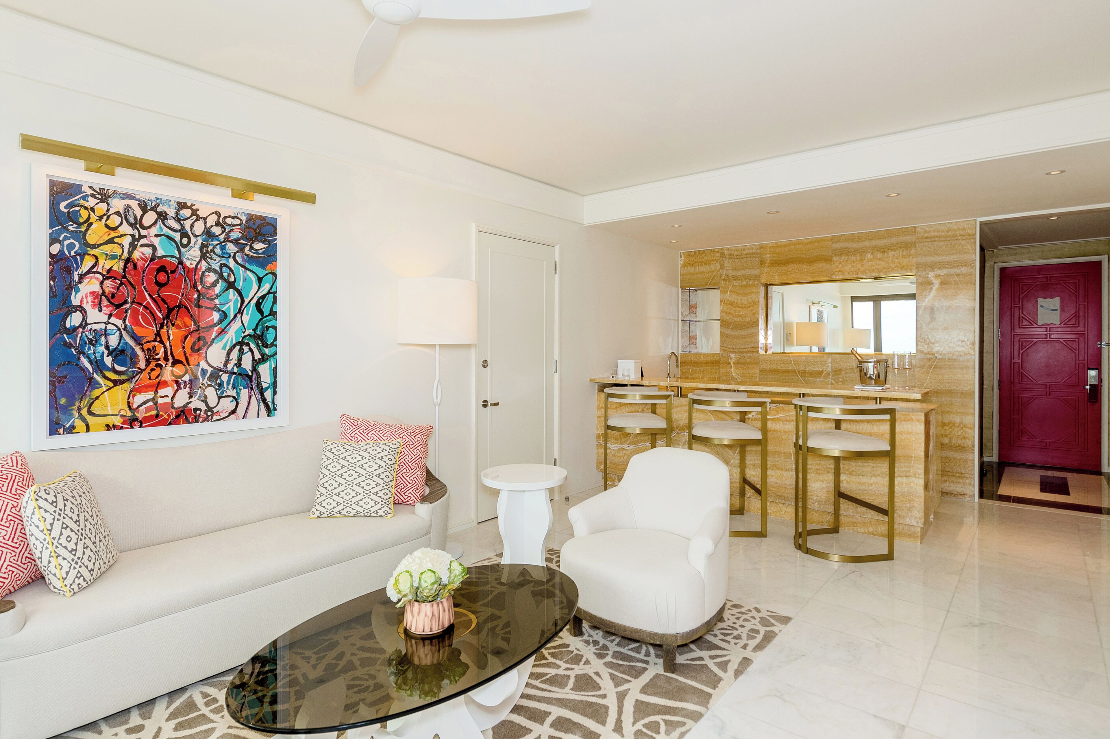 A modern living room with a white sofa, a glass coffee table, and a colorful abstract painting.