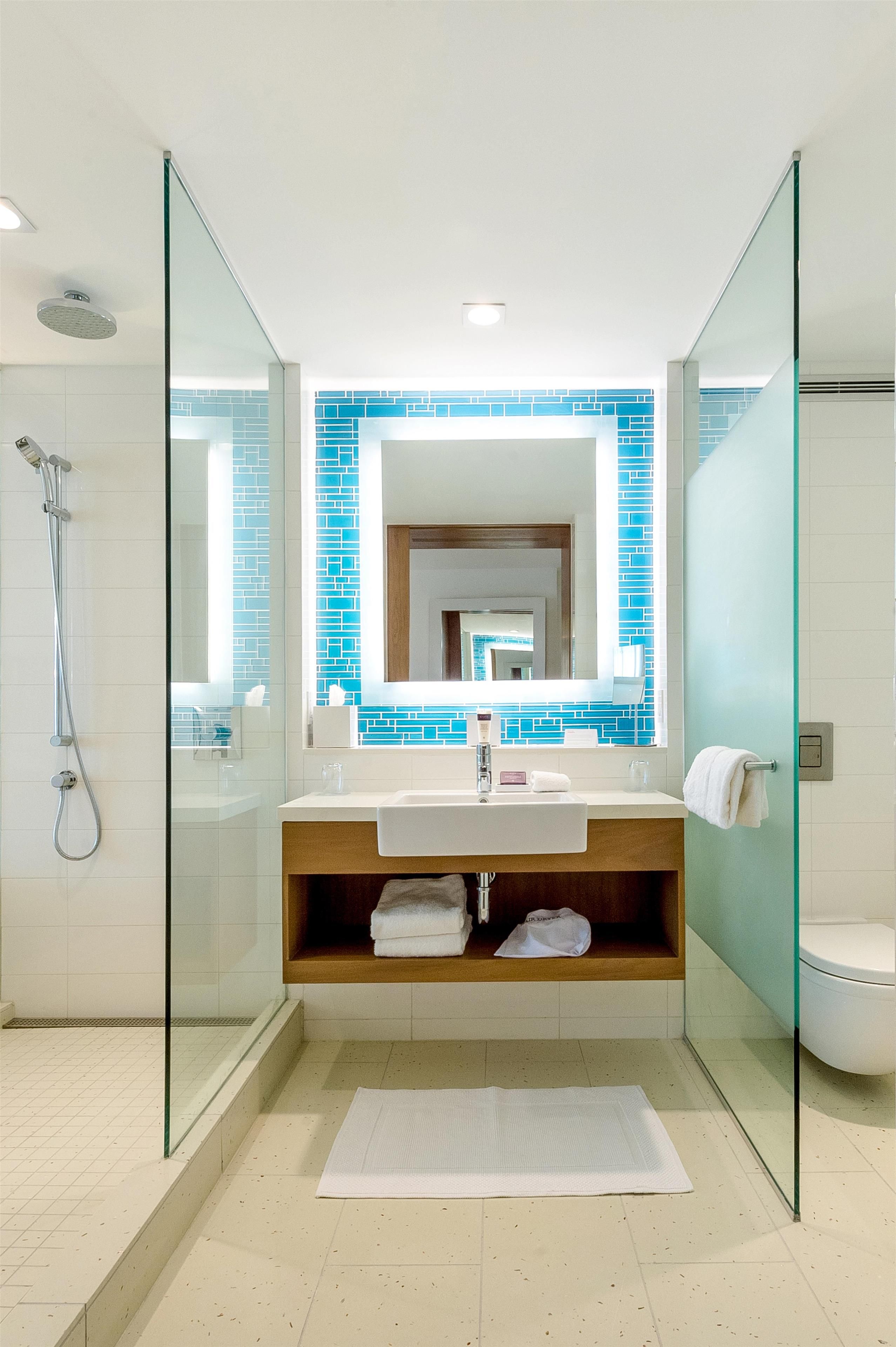 A modern bathroom with a glass shower enclosure, a white sink with a wooden vanity, and a blue-tiled backsplash.
