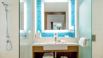 A modern bathroom with a glass shower enclosure, a white sink with a wooden vanity, and a blue-tiled backsplash.