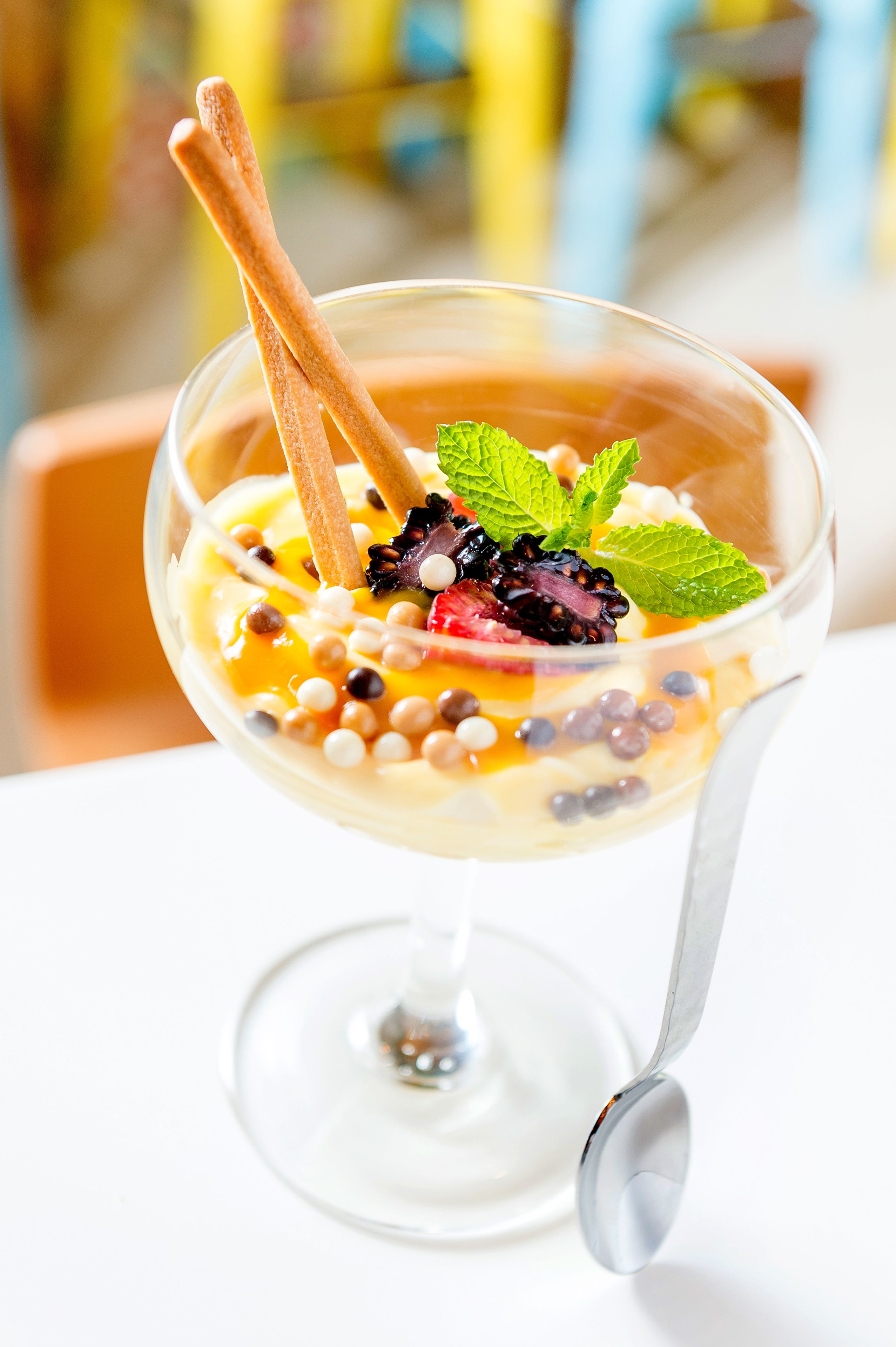 Un dessert servi dans un verre transparent, accompagné d’une cuillère, et décoré de feuilles de menthe et de baies.
