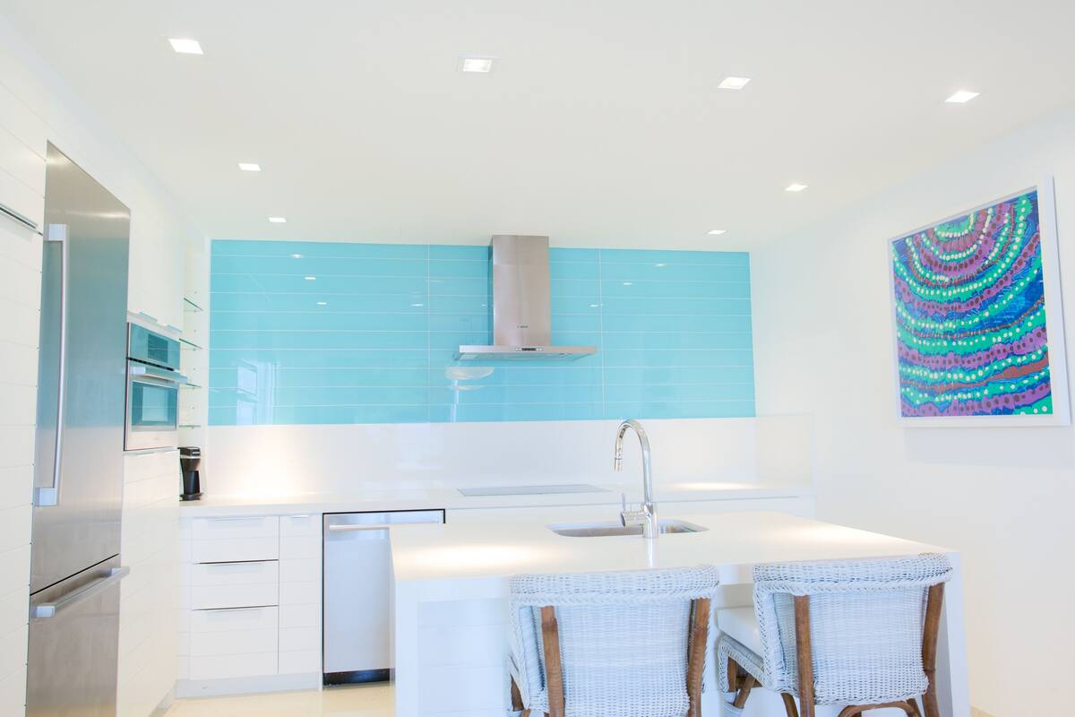 Cocina moderna con una isla central, muebles blancos y salpicadero azul.