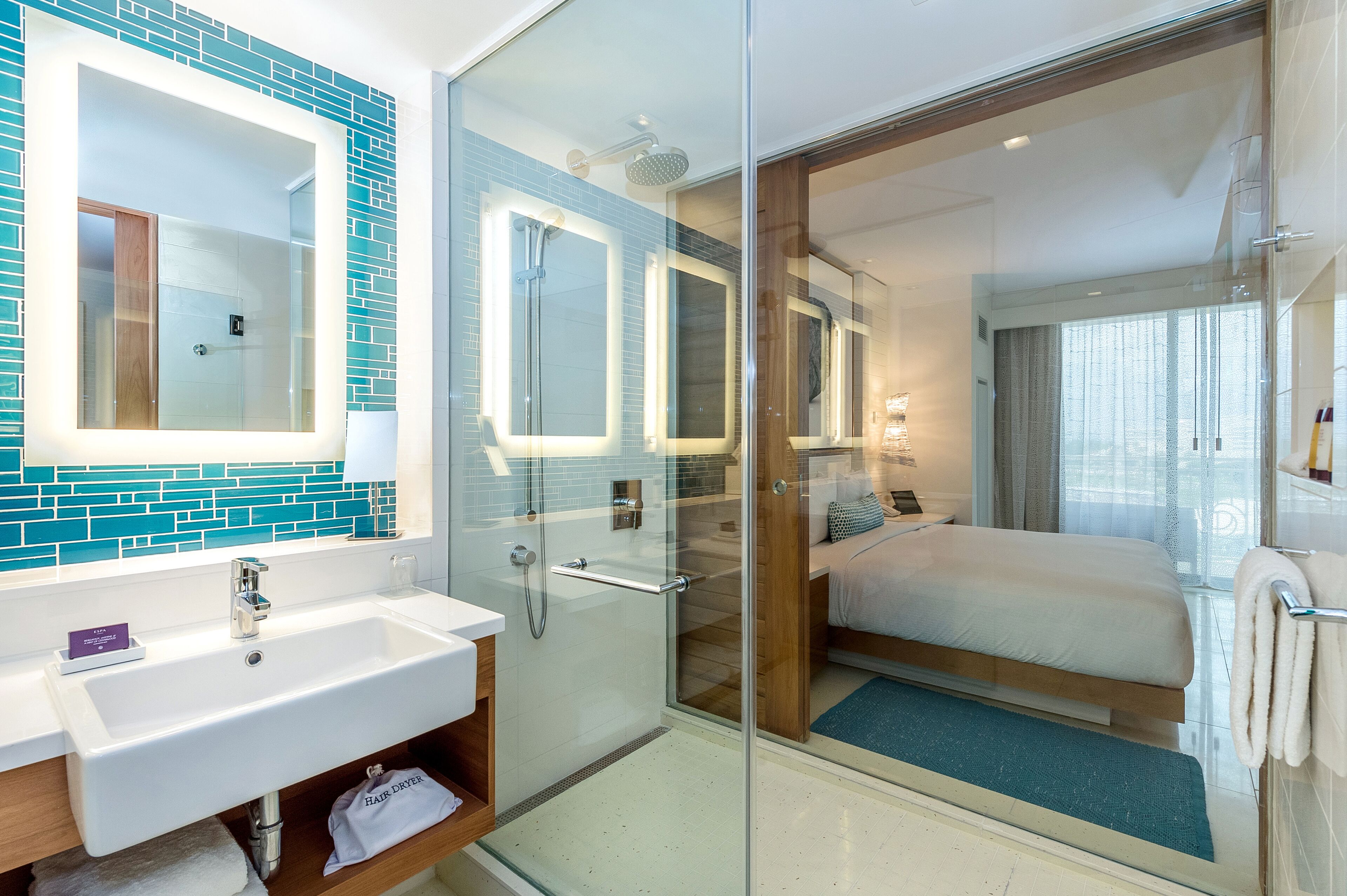 A modern hotel bathroom with a glass-enclosed shower, a large mirror, and a separate sink area.