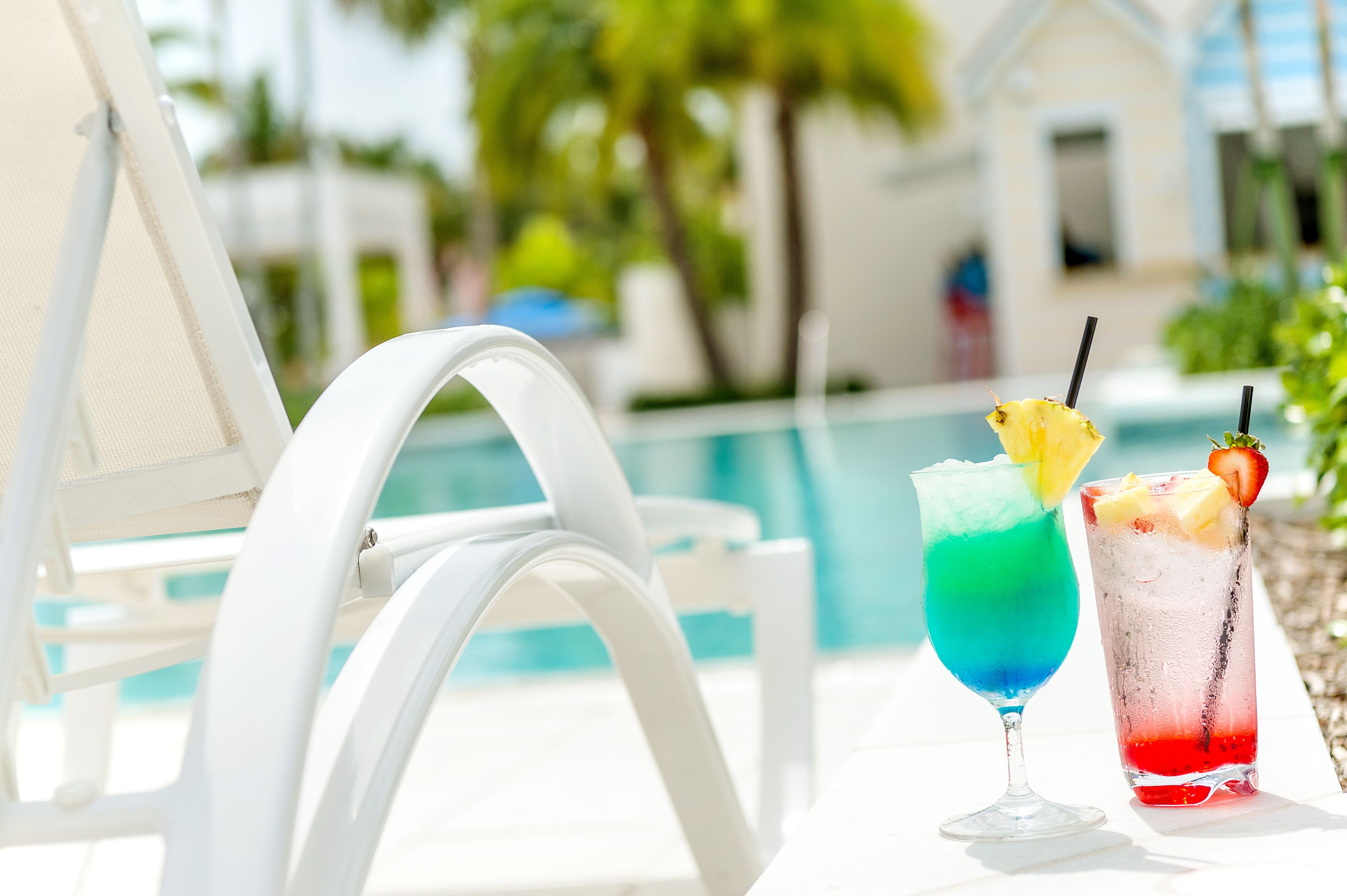 A poolside setting with two colorful cocktails and a white lounge chair.