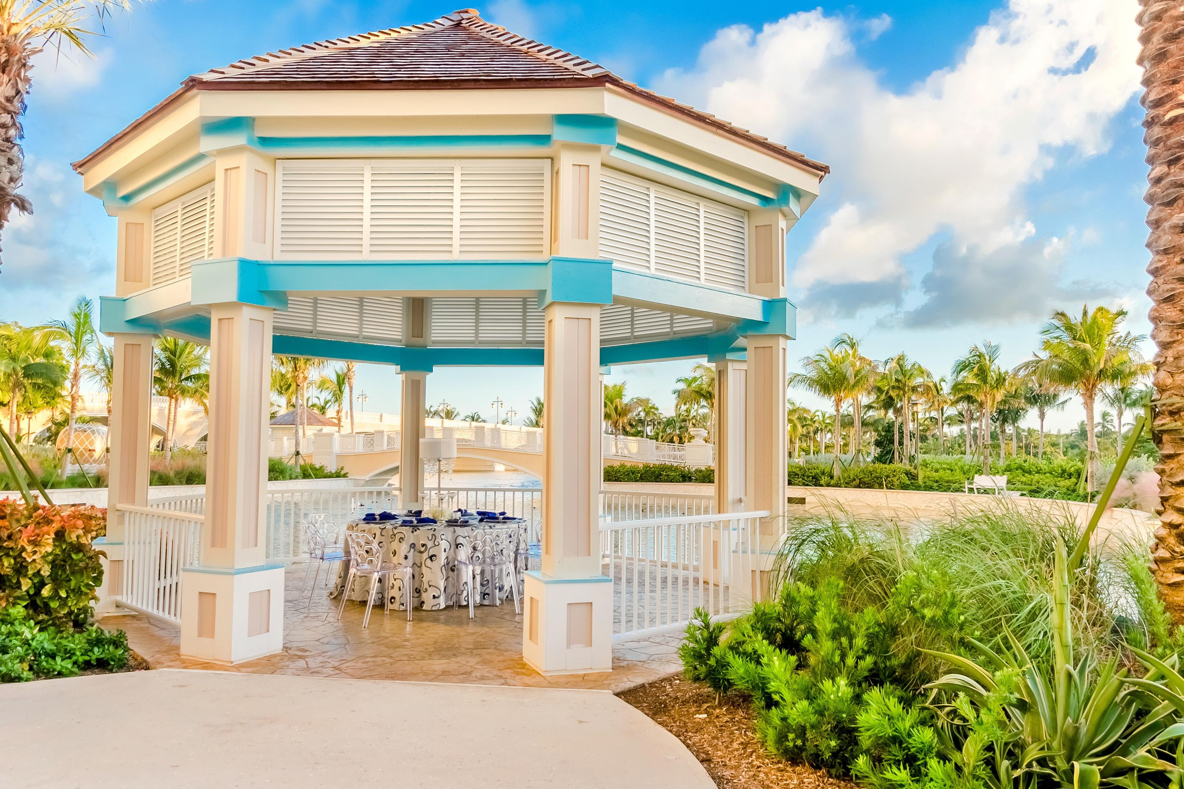 A gazebo with a white and blue color scheme, surrounded by palm trees and a pool area.