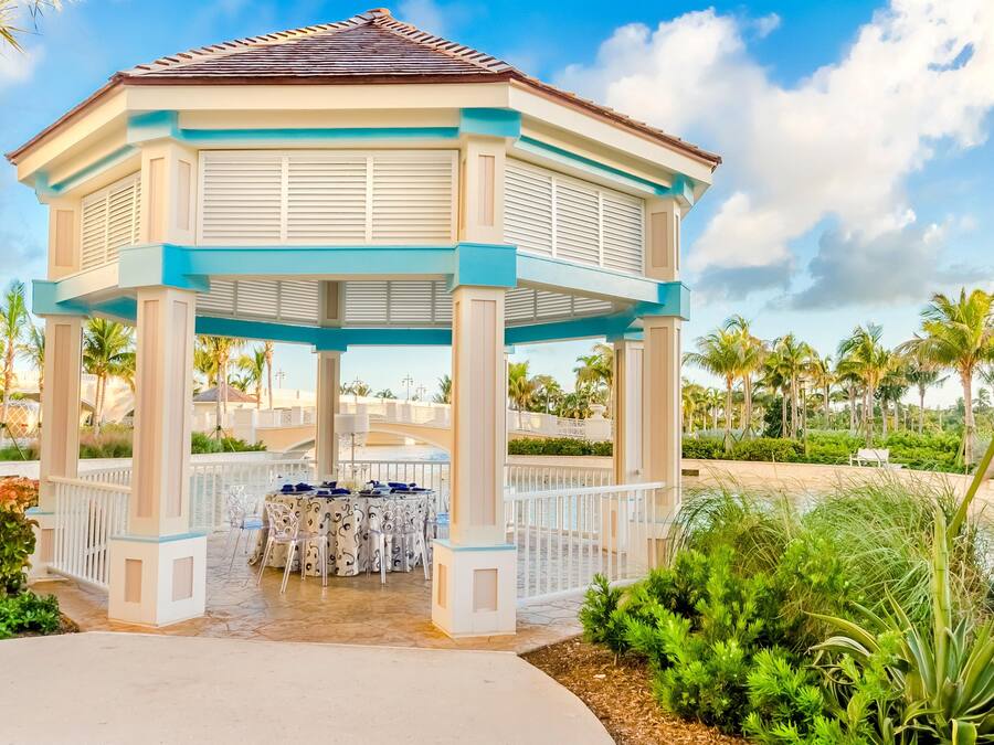 A gazebo with a white and blue color scheme, surrounded by palm trees and a pool area.