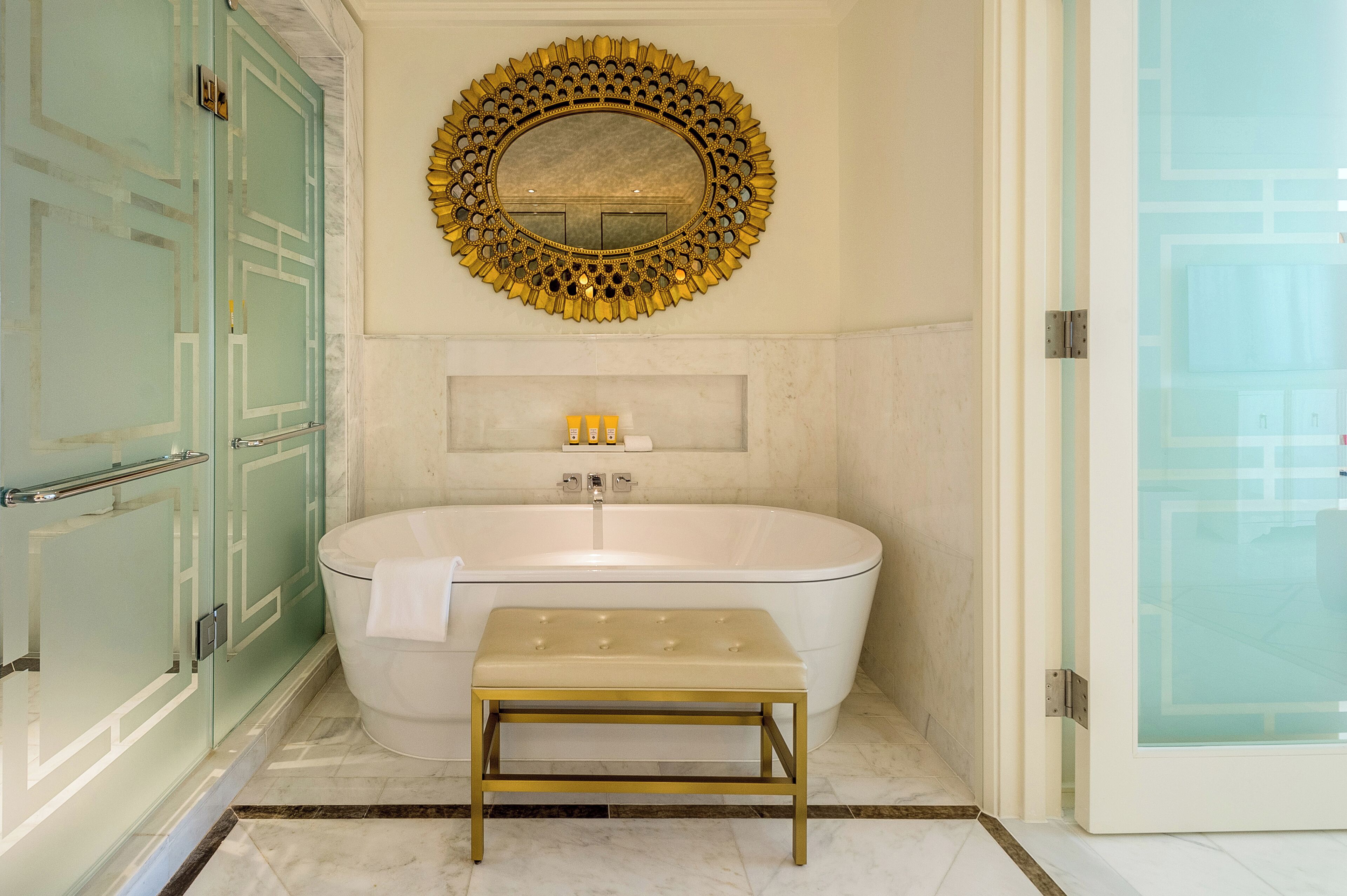 Une salle de bain avec une baignoire sur pieds, un miroir encadré d’or et une douche séparée par des parois de verre.