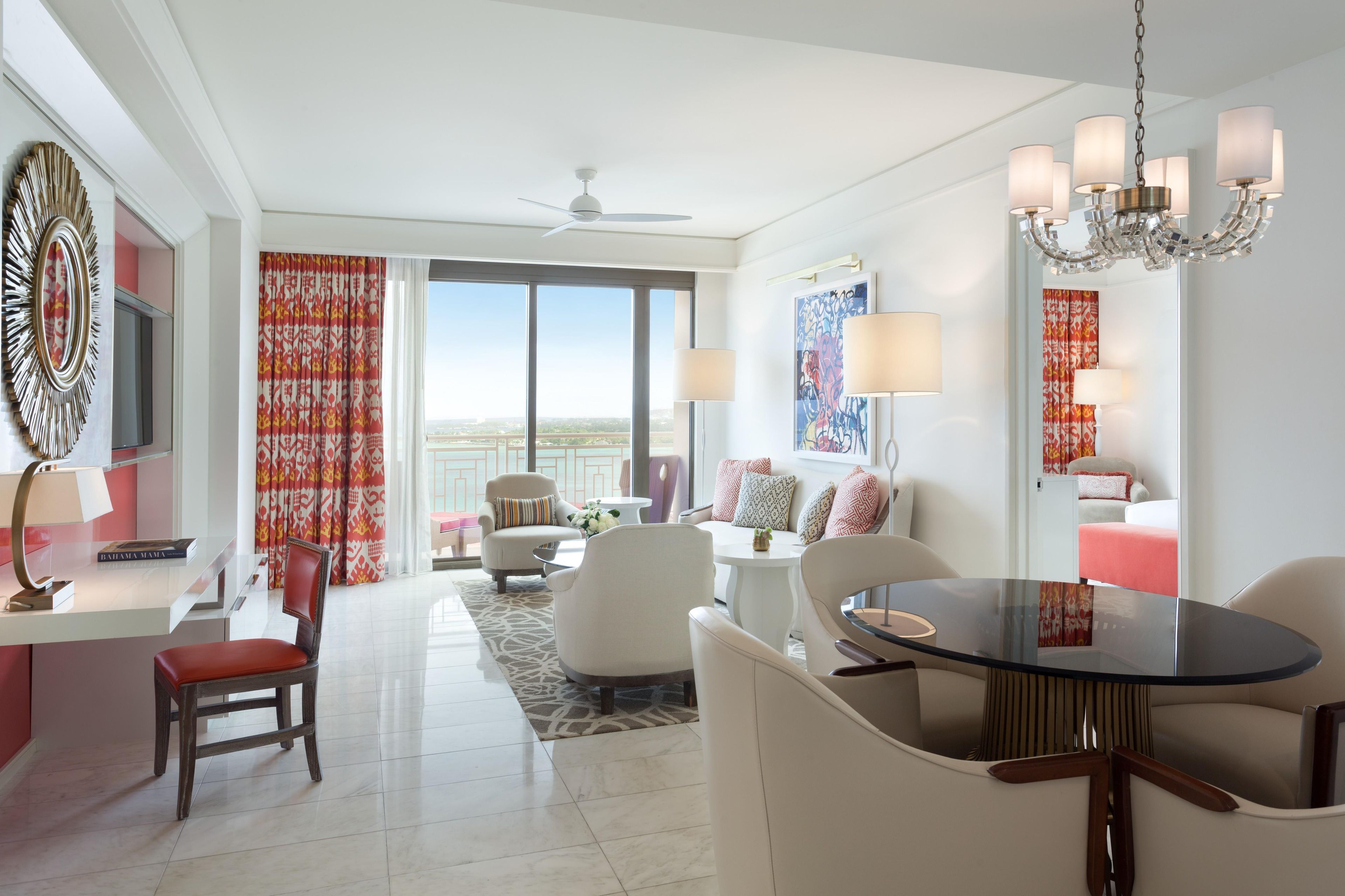 A modern hotel room with a dining area, a large window with a view, a ceiling fan, and a chandelier.