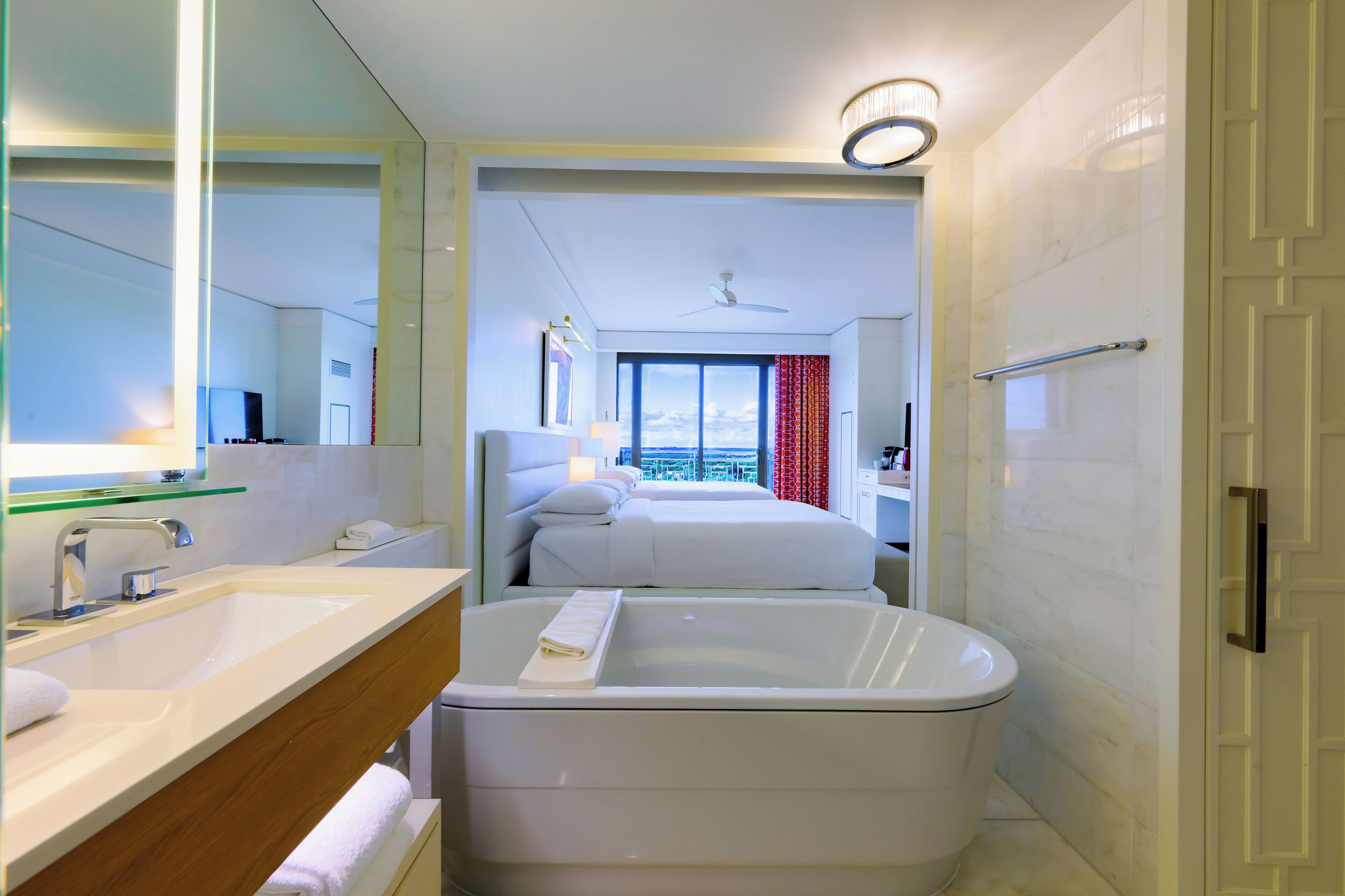 Une salle de bain moderne avec une baignoire, un meuble-lavabo avec un miroir et une grande fenêtre offrant une vue sur la ville.
