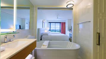 Une salle de bain moderne avec une baignoire, un meuble-lavabo avec un miroir et une grande fenêtre offrant une vue sur la ville.