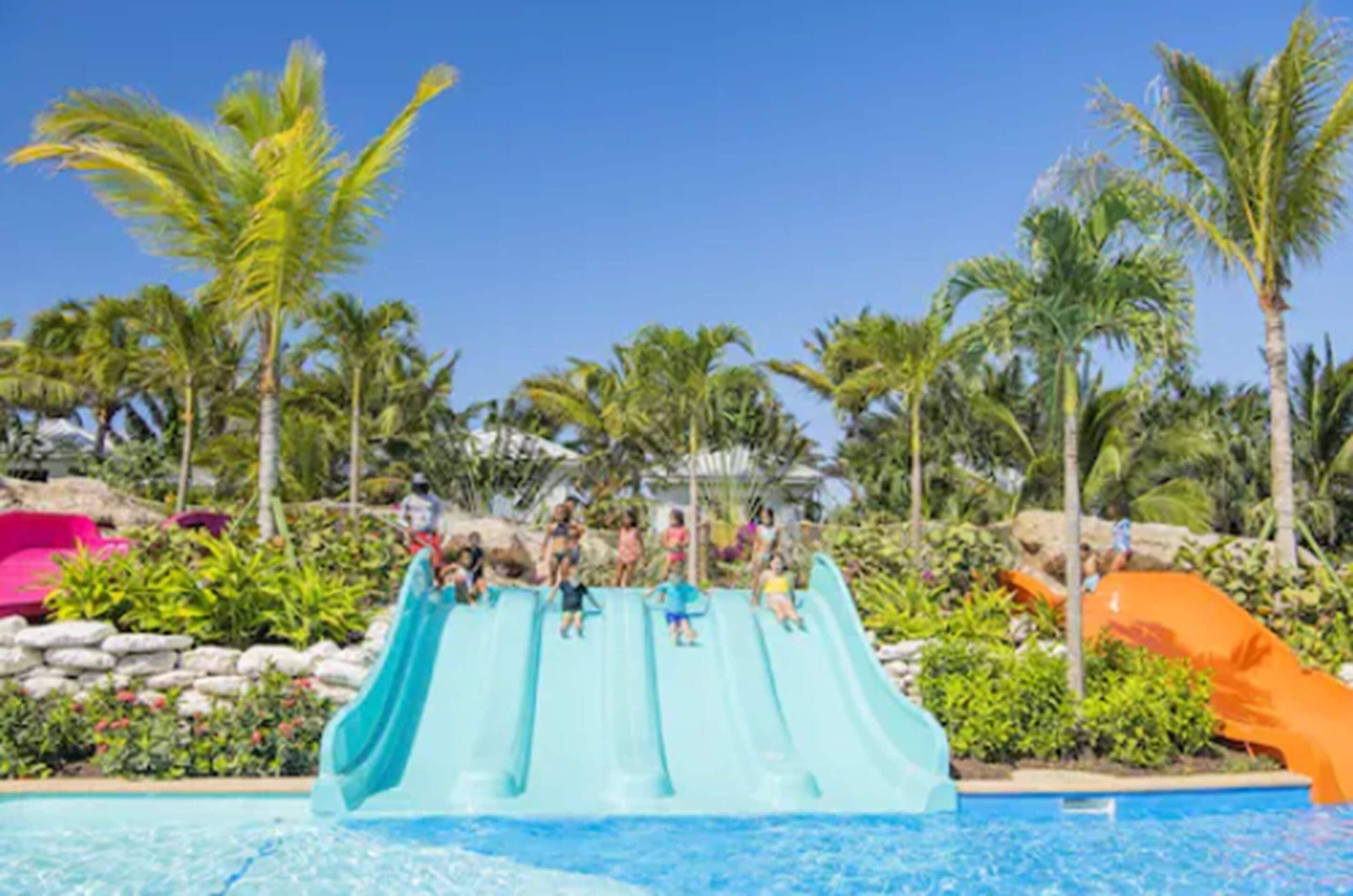 Um toboágua em um resort com piscina, palmeiras e céu claro.