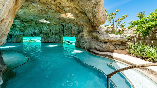 A natural pool with clear blue water, surrounded by rock formations and greenery.