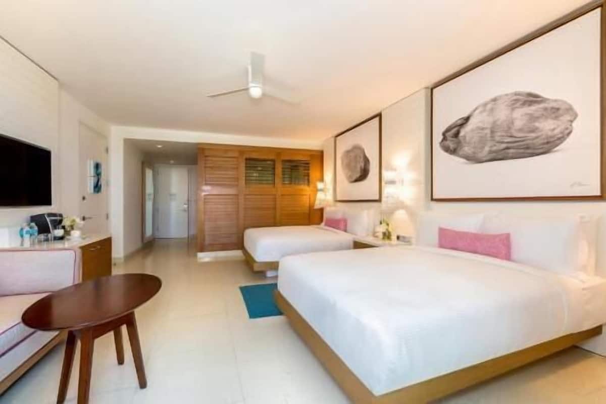 Habitación de hotel con dos camas, un escritorio, una silla, un televisor y obras de arte en las paredes.