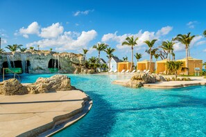 A resort pool area with clear blue water, palm trees, and a rocky backdrop. - Grand Hyatt Baha Mar (Nassau)