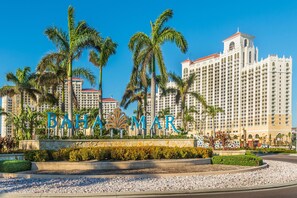 Un grand hôtel, reconnaissable à son enseigne bien visible où l’on peut lire « BAHAM MAR », entouré de palmiers et surplombant un ciel d’un bleu limpide.