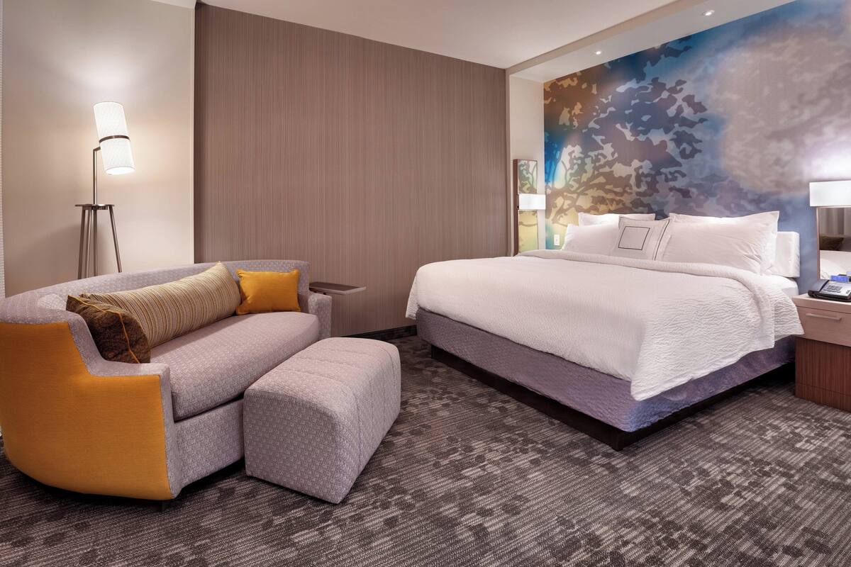 A hotel room with a large bed, a sofa, a small table, and a floor lamp.