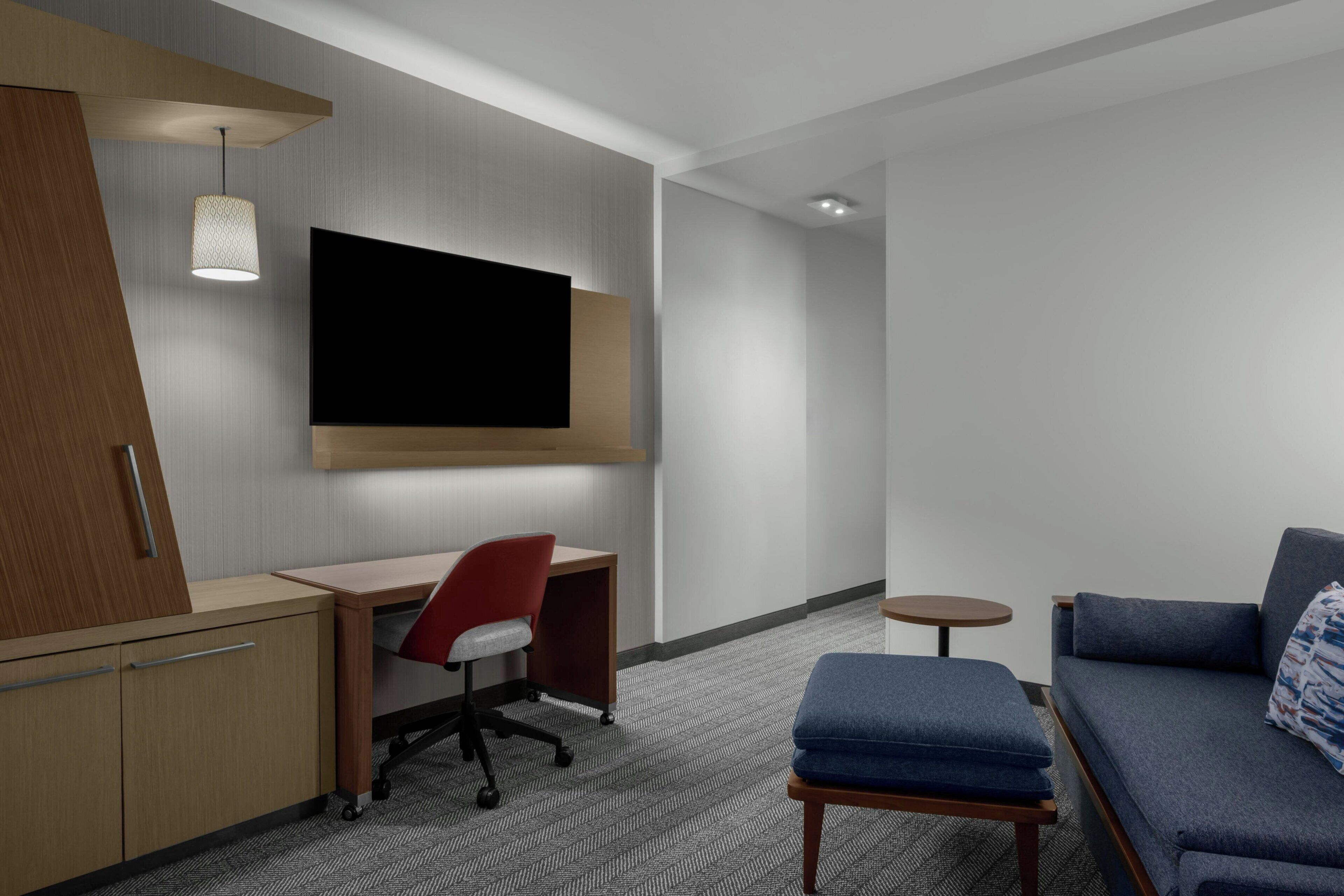 Habitación de hotel con escritorio, silla, televisor, sofá y una mesita.