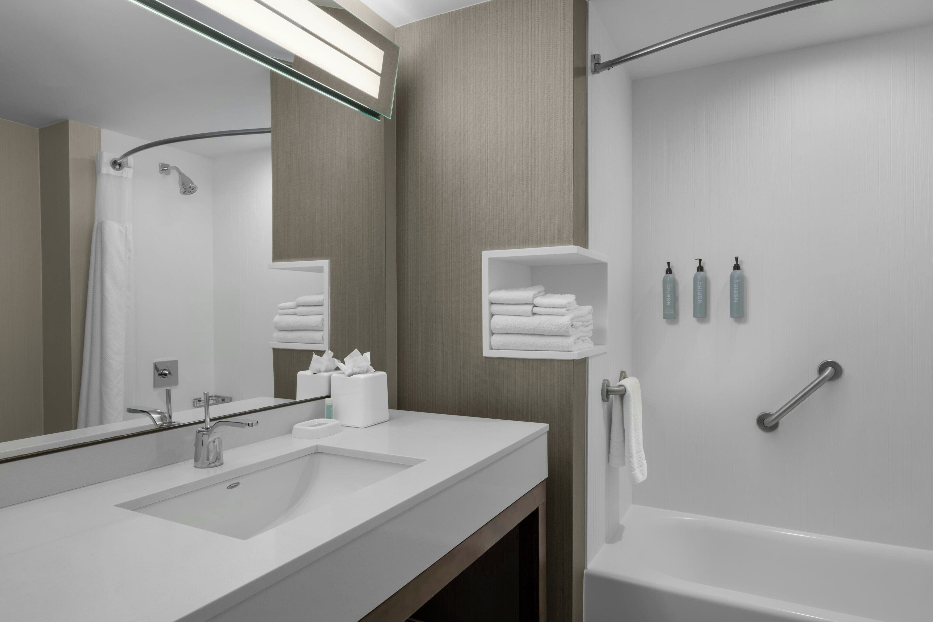 Un baño moderno con un espejo grande, un lavabo, una ducha y un perchero para toallas.