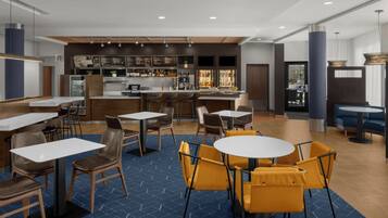 Un ristorante moderno con zona bar, varie opzioni di posti a sedere tra cui tavoli rotondi e sgabelli da bar, e un pavimento a motivi blu.