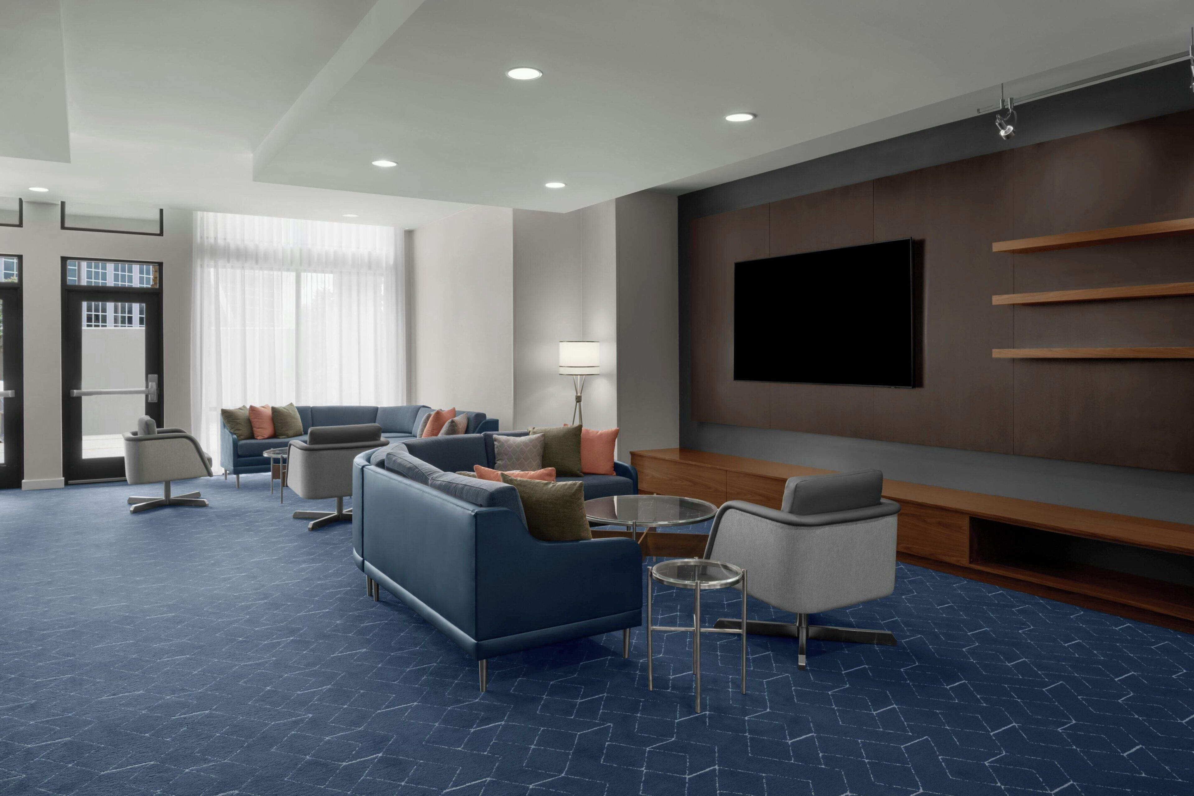 A modern hotel room with a sofa, armchairs, a TV, and a lamp.
