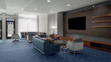 A modern hotel room with a sofa, armchairs, a TV, and a lamp.