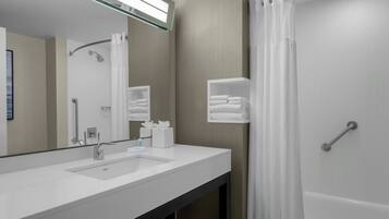 Une salle de bain moderne avec un grand miroir, un lavabo blanc, des porte-serviettes et un espace douche.