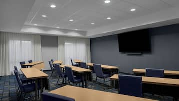 A conference room with multiple tables and chairs, a large screen on the wall, and a ceiling with recessed lighting.
