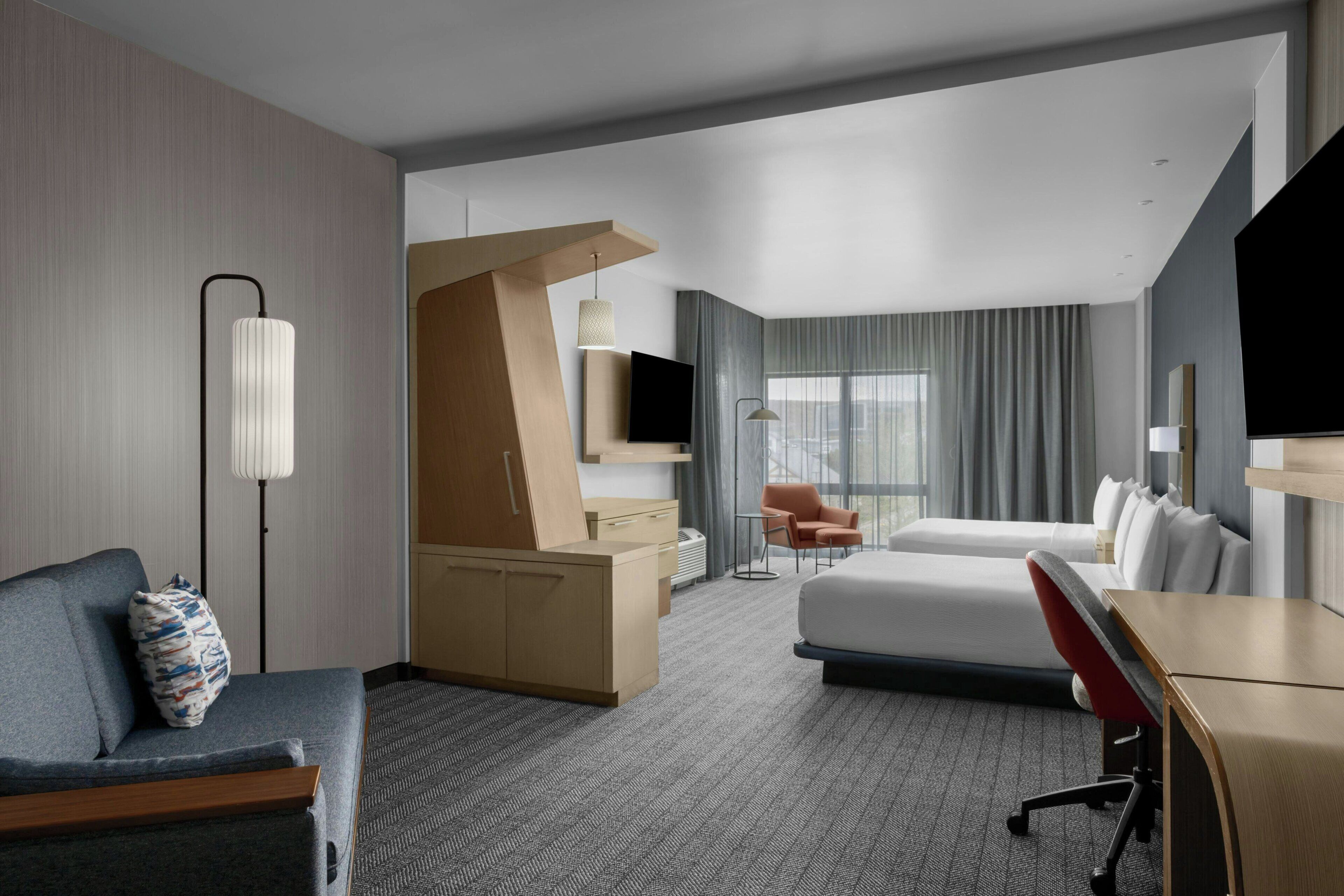 A modern hotel room with a bed, a desk, a chair, a sofa, and a TV.